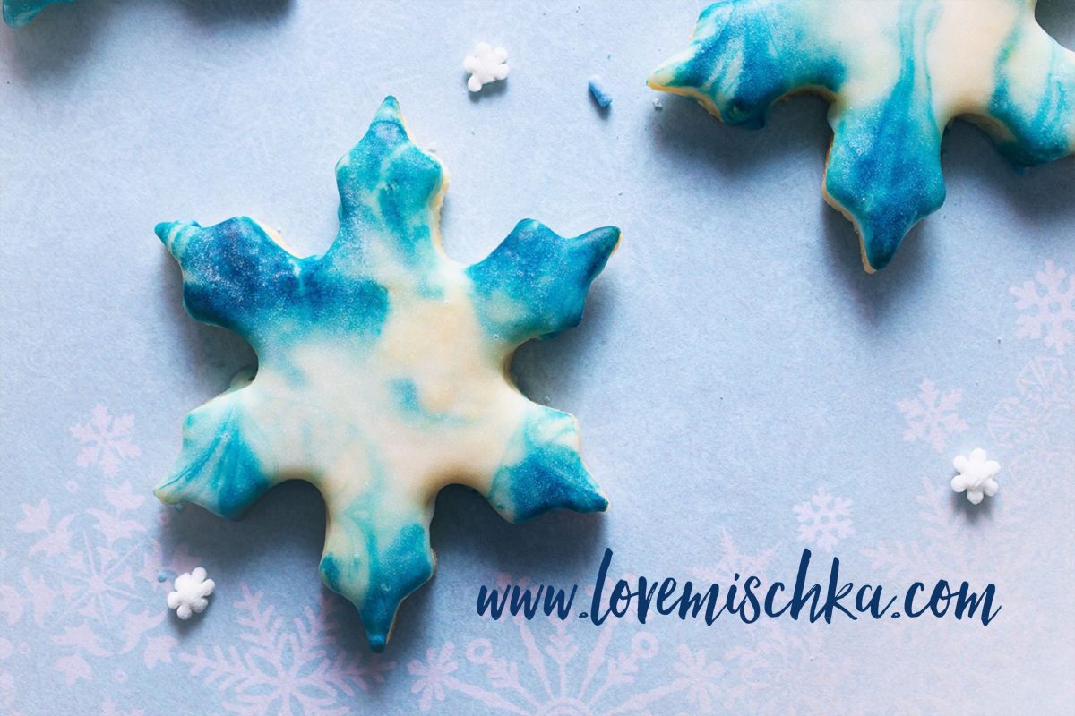 A blue and white snowflake sugar cookie surrounded by white snowflake sprinkles.