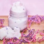 Fluffy white sugar scrub with pink and white sprinkles in a mason jar on a piece of wood with pink and purple confetti.