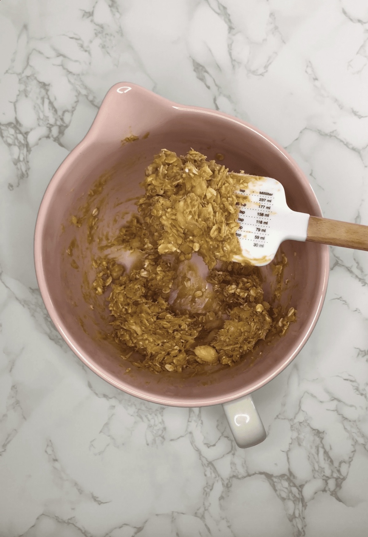 The brown batter for Peanut Butter Banana Dog Treats in a pink mixing bowl and on a white spatula