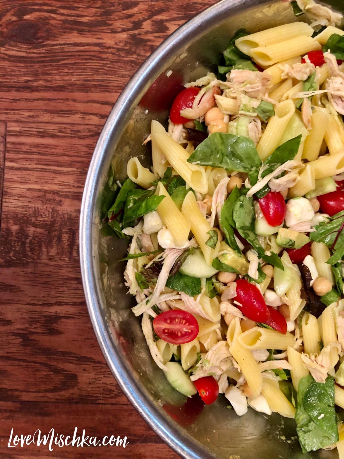 A bowl of pasta, tomatoes, chicken, basil, chickpeas, cucumbers, mozzarella, and more.