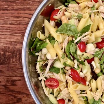 A big bowl of healthy, gluten-free pasta salad with lots of vegetables like red tomatoes, green lettuce. It also includes white mozzarella cheese and tan chickpeas.