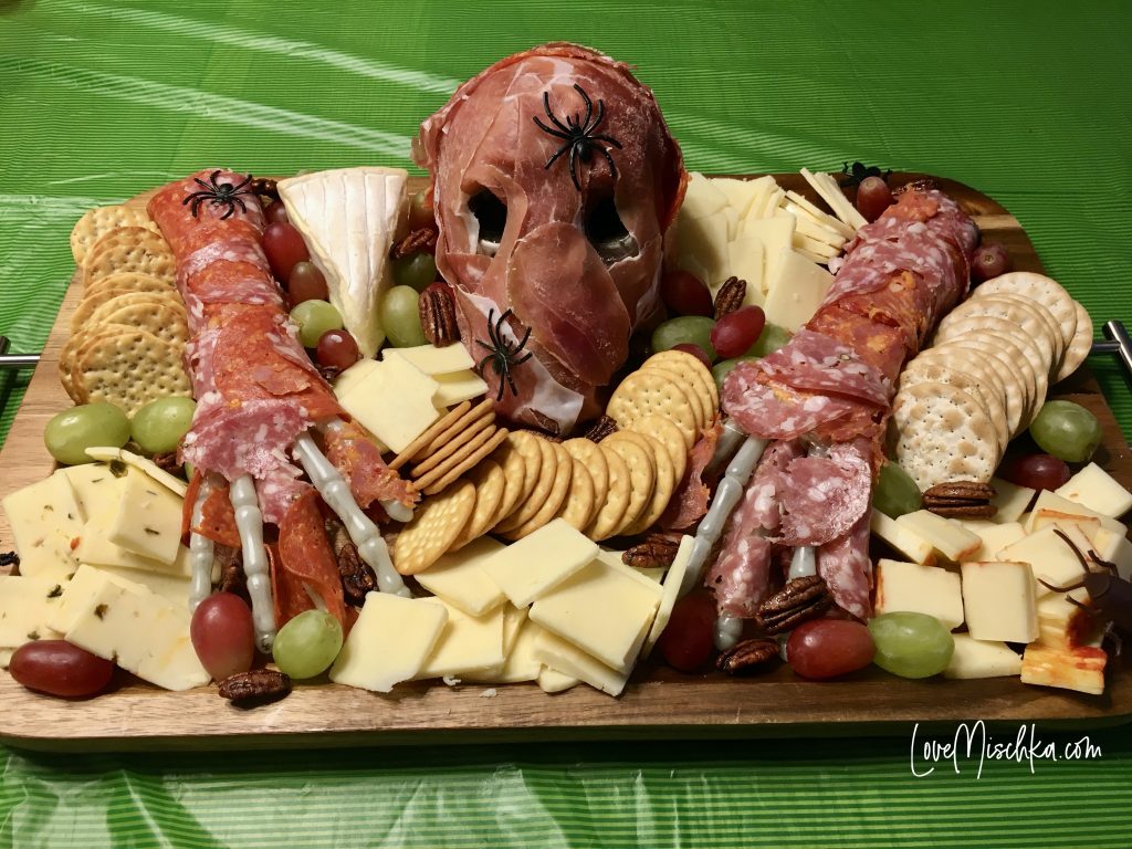 Halloween Charcuterie Board with a Spooky Skeleton Covered in different meats to look like rotten skin and surrounded by cheese covered in toy bugs and pecans.