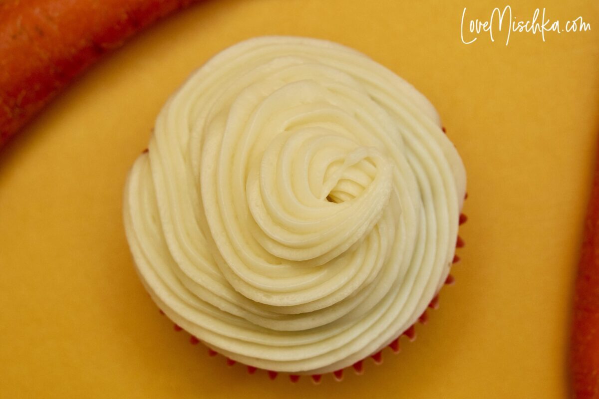 White Silky Cream Cheese Frosting swirled on top of a carrot cake cupcake.