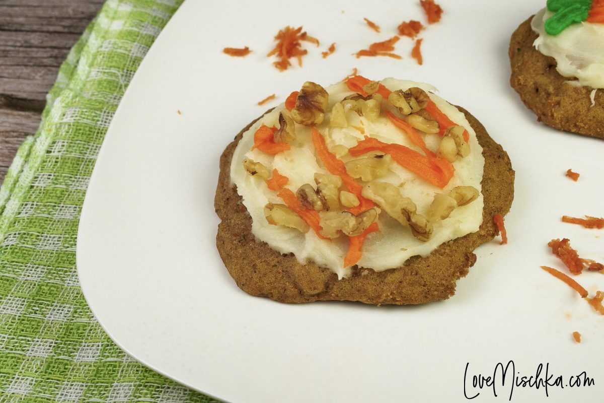 A Carrot Cake Cookie with orange cream cheese frosting striped across white cream cheese frosting and topped with chopped walnuts.