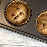 Golden Banana Bread Chocolate Chip Muffins, freshly baked, are still in a silver baking pan.