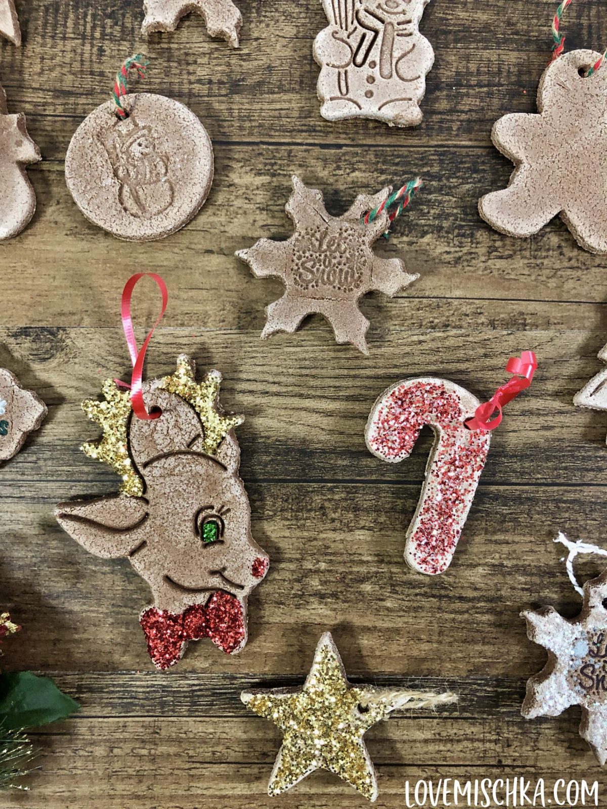 Many light brown cinnamon salt dough ornmanets on a piece of wood. Some have red and gold sparkles.