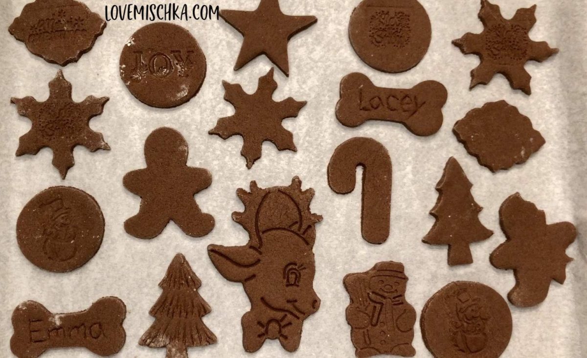 Brown holiday-shaped cinnamon salt dough ornaments on a piece of parchment paper before being baked.