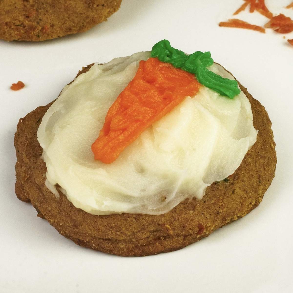 A brown carrot cake cookie topped with white cream cheese frosting (and an orange carrot).