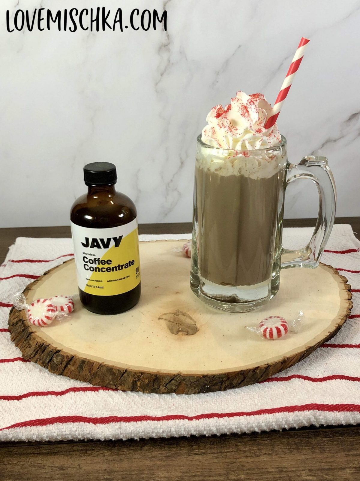 A bottle of Javy Coffee Concentrate next to a big glass of Peppermint Mocha topped with whipped cream and red sanding sugar. 