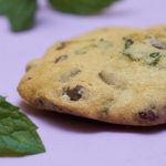 A chocolate chip cookie with fresh mint sits next to bright green mint leaves.