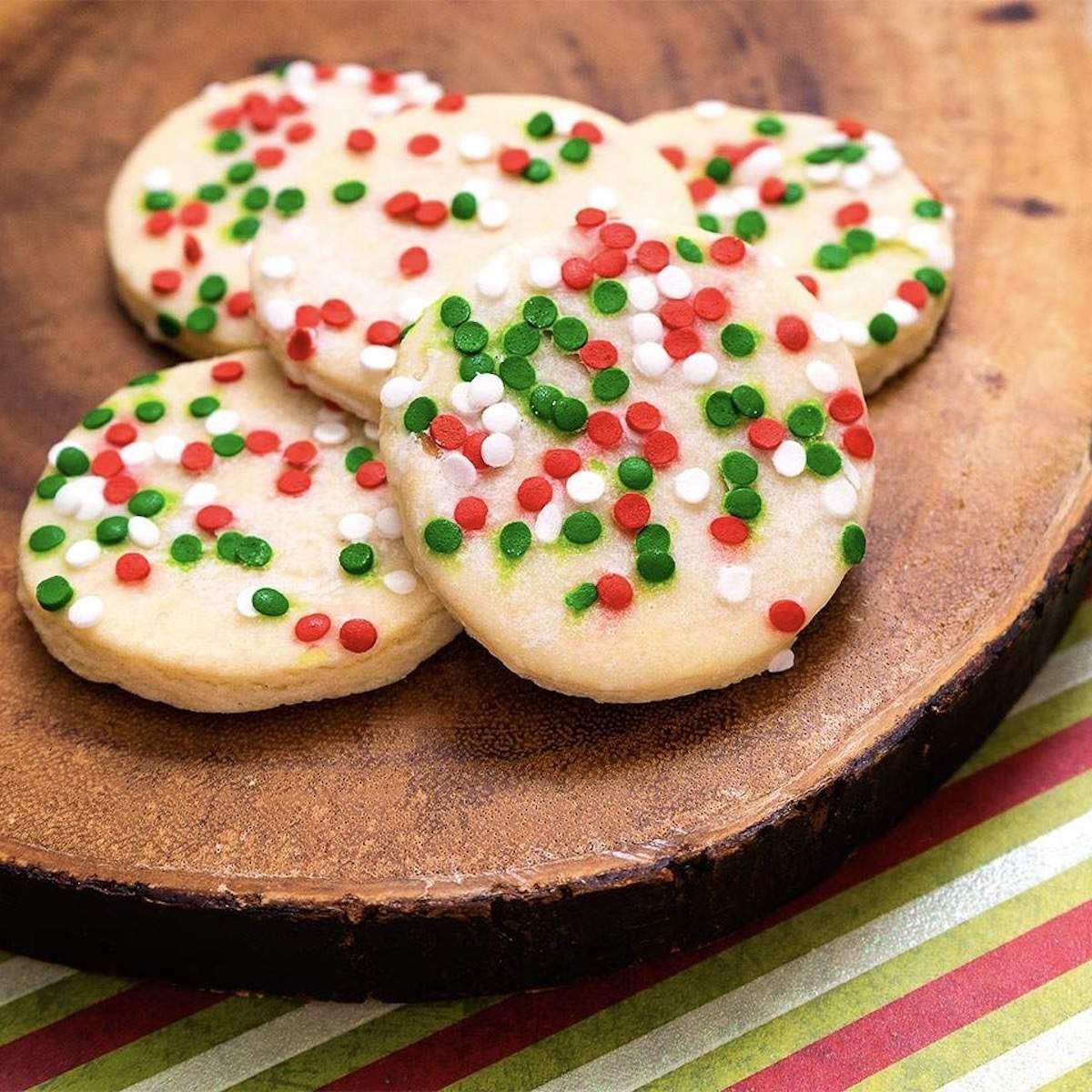 Round sugar cookies with red, green, and white sprinkles sit on a wooden board.