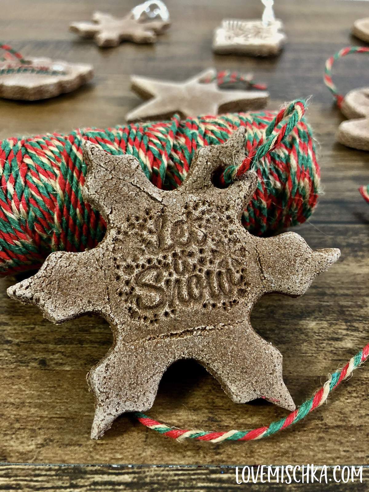 A snowflake-shaped brown cinnamon salt dough ornament laying on a roll of red, gold, and green twine.