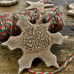 A snowflake-shaped brown cinnamon salt dough ornament laying on a roll of red, gold, and green twine.