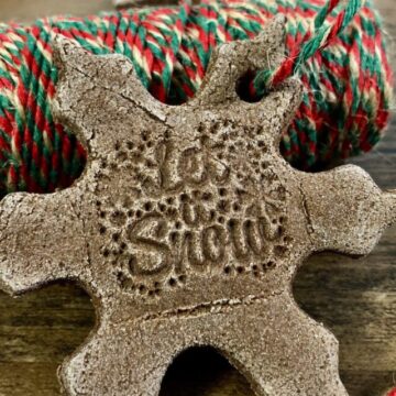 A snowflake-shaped brown cinnamon salt dough ornament laying on a roll of red, gold, and green twine.