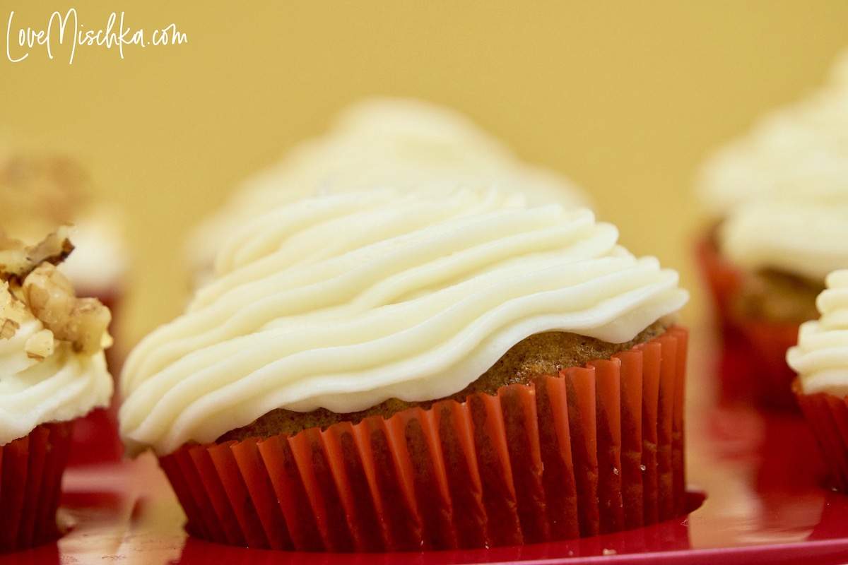 A closeup of the best carrot cake cupcakes with creamy, silky, white cream cheese frosting in a red cupcake caddy.