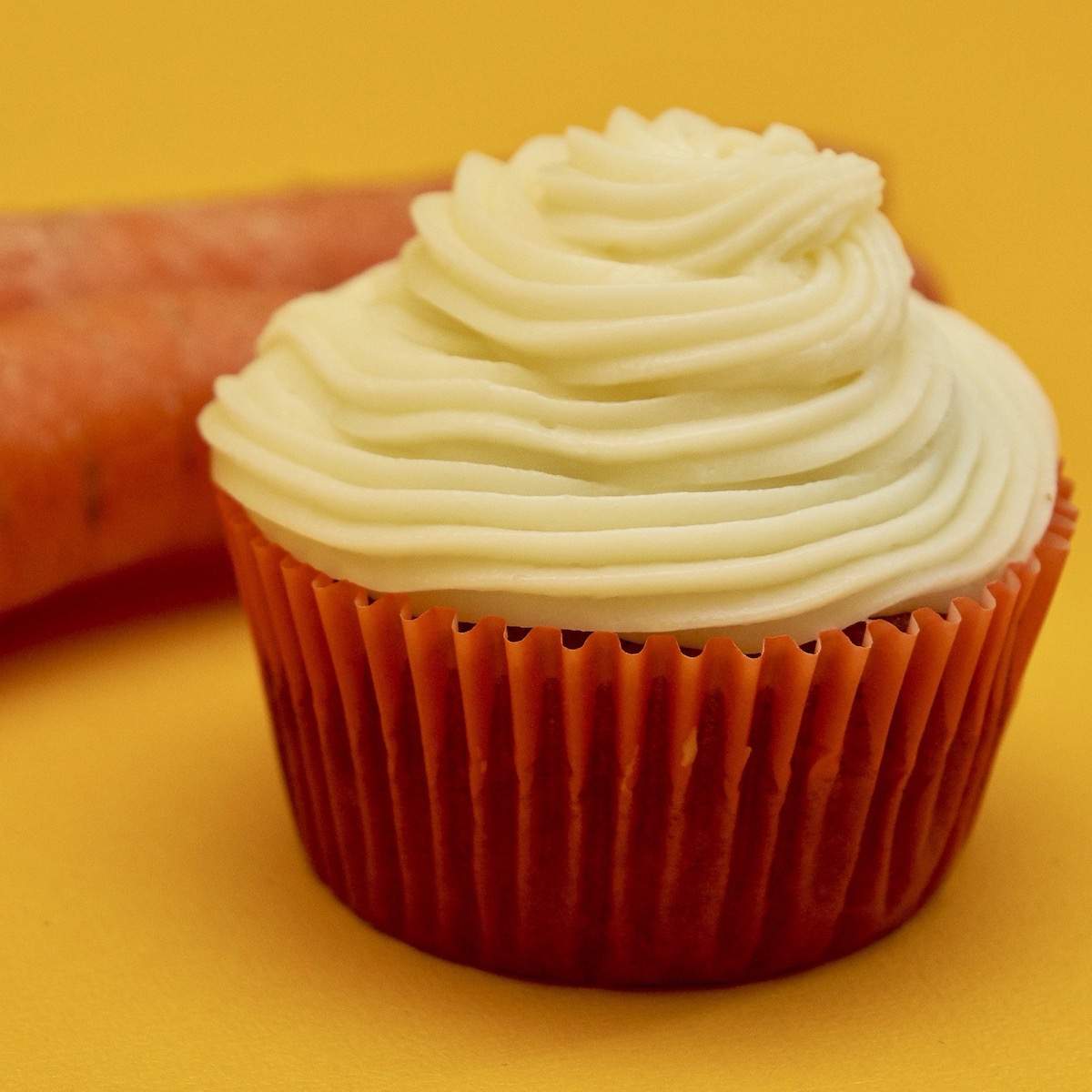 One carrot cake cupcake in a dark orange cupcake liner topped with white silky cream cheese frosting