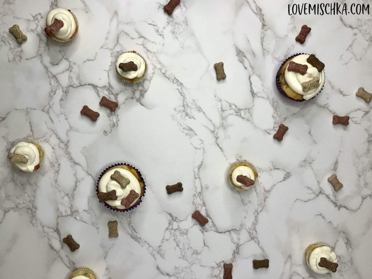 Varying sizes of Bacon Cheddar Pupcakes on a marble surface, surrounded by tan, brown, and red mini bones.