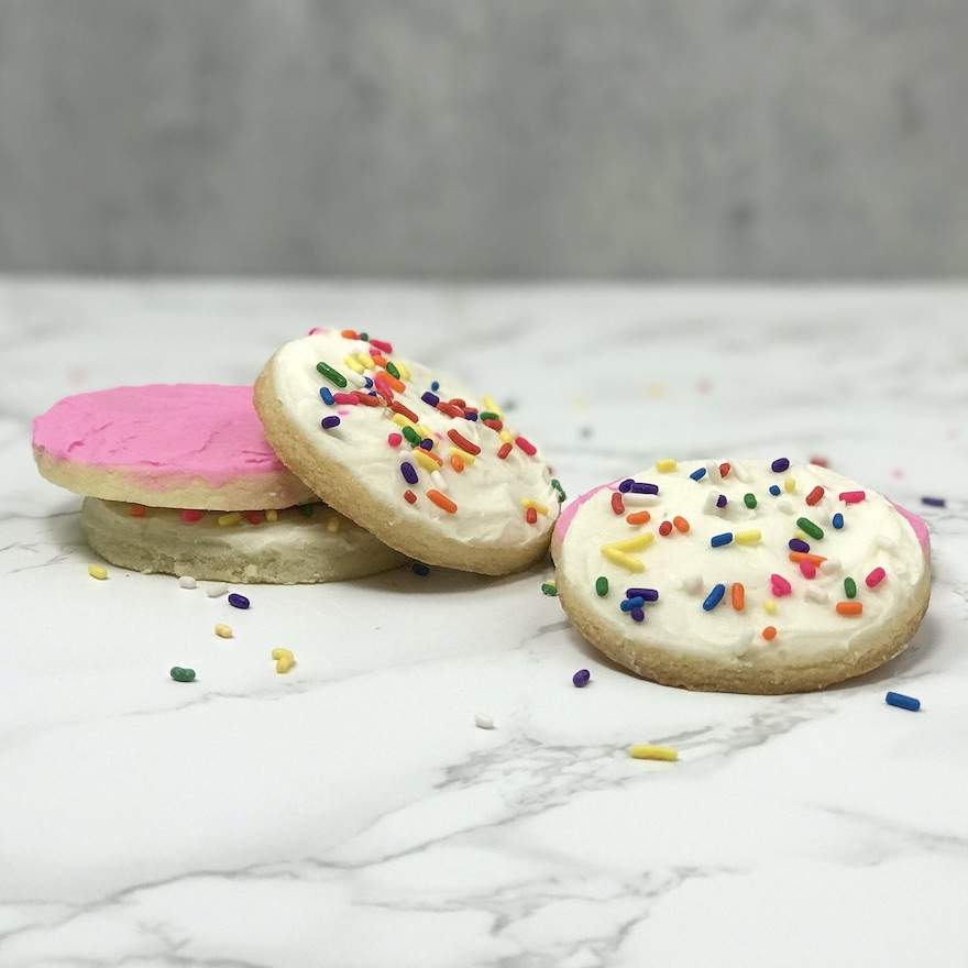 Soft Sugar Cookies with white and pink buttercream frosting and sprinkles lay on one another on a marble countertop.