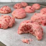 A pink cherry cookie with a bite taken out of it to reveal bright red pieces of cherry and a moist crumb inside.