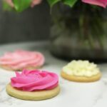 Three round sugar cookies with pink and white buttercream frosting on top to look like roses and a flower.