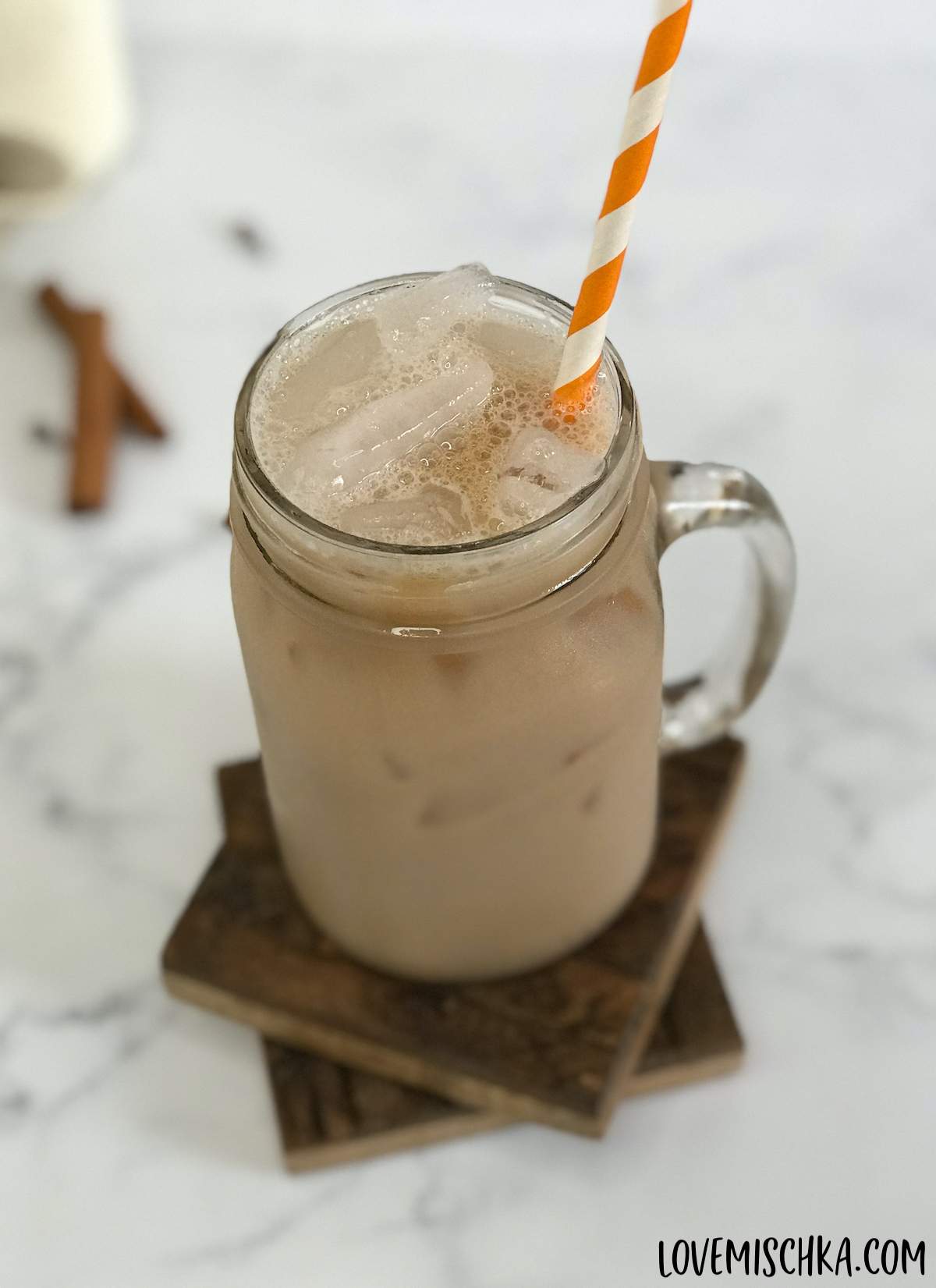 A tan Starbucks chai tea latte iced in a mason jar glass with an orange and white striped straw. 