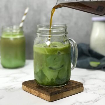 Brown Brewed Instant Coffee is carefully poured into a mason jar glass of matcha tea and milk, creating beautiful swirls of white milk, green matcha, and brown coffee.