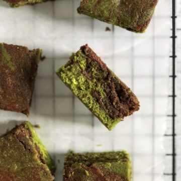 A bright green and dark brown swirled matcha brownie on its side on white parchment paper.