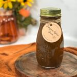 A glass mason bottle full of dark brown pumpkin sauce for coffee in How to Make Pumpkin Sauce for Coffee. The neck is wrapped with tan twine that secures a circular, peach label that says, "Pumpkin Spice Syrup".