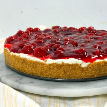 The layers of a no bake cherry cheesecake - bright red cherry pie filling on top of white cheesecake filling, which is on top of a golden graham cracker crust.
