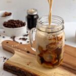 Creamy, beige oatmilk poured into a mason jar glass of dark brown espresso, creating beautiful swirls of different shades of browns and tans.
