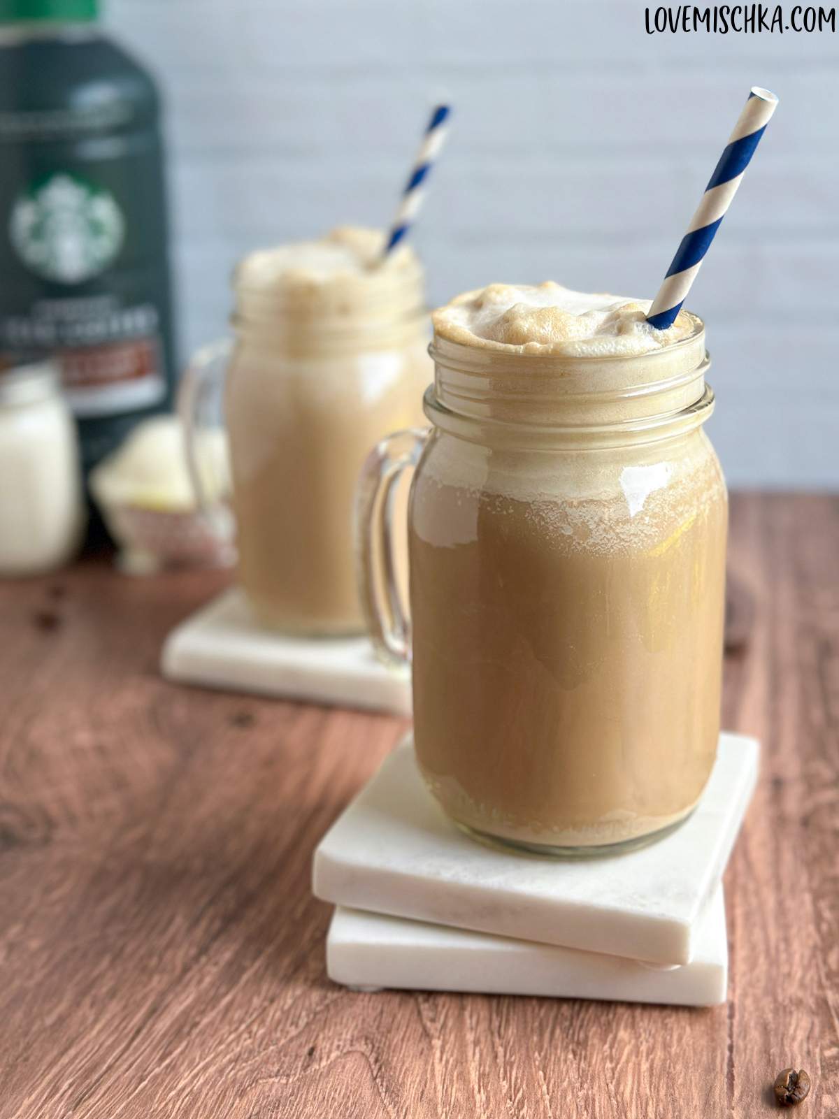 A mason jar glass filled with cold coffee with ice cream, in front of another iced coffee with ice cream and the three ingredients of this simple recipe. 