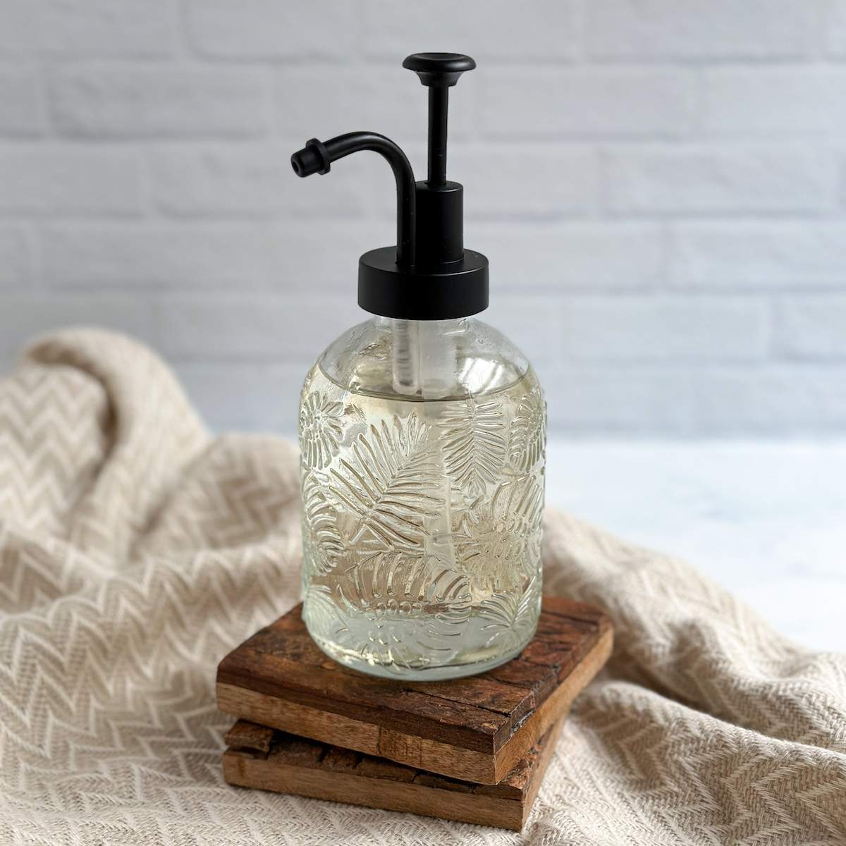 Clear simple syrup sits in a beautiful syrup dispenser with a black pump, on top of two wooden coasters.
