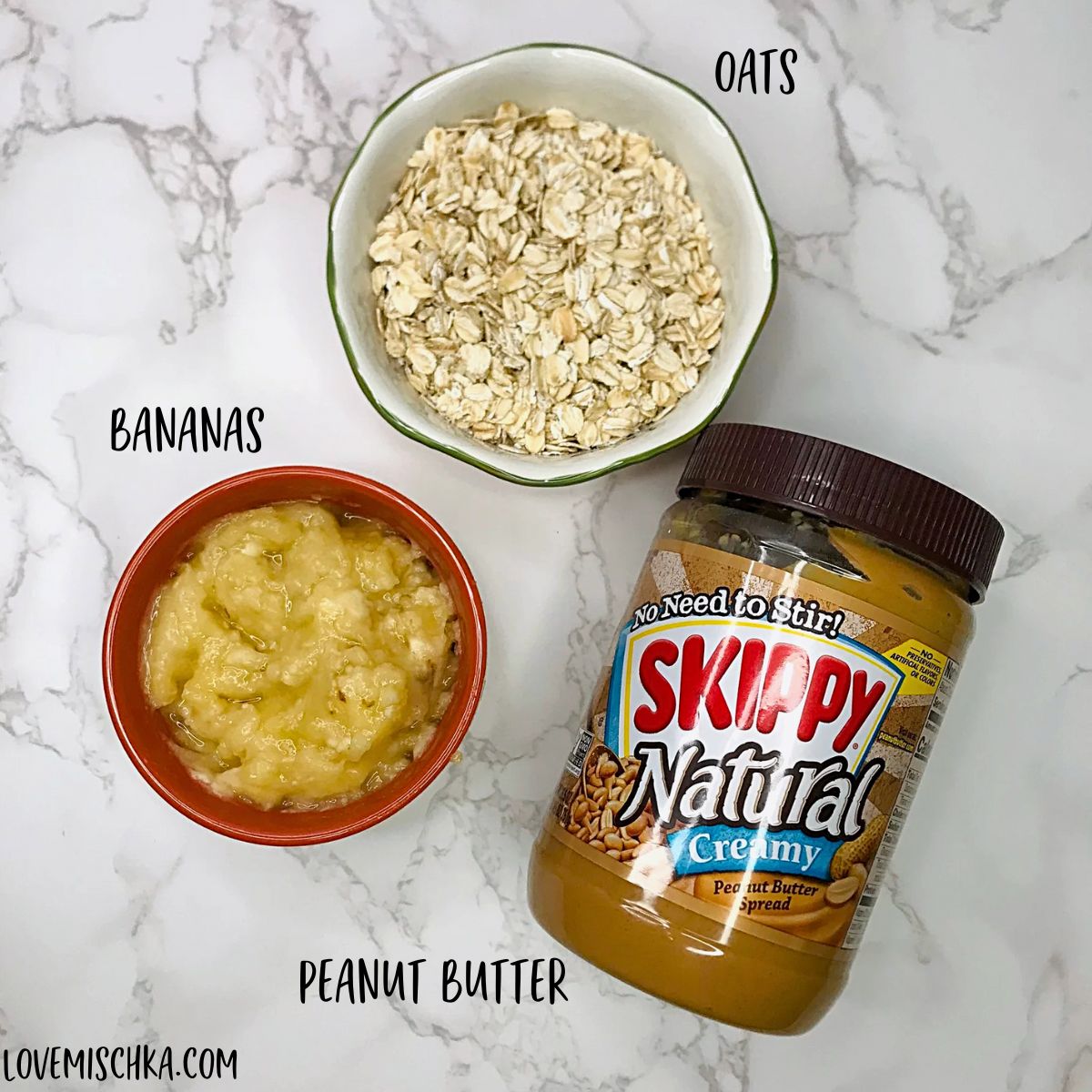 The three ingredients needed for this Peanut Butter Banana Dog Treats Recipe - a small bowl of yellow mashed bananas, a small bowl of old-fashioned oats, and a jar of Skippy Natural peanut butter.