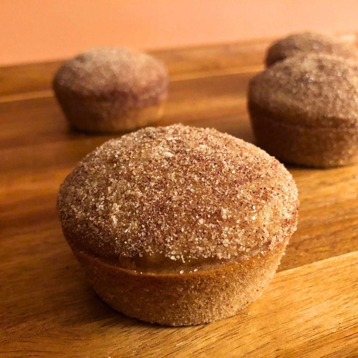 Fluffy, tan Apple Cider Donut Muffins with a cinnamon sugar topping sit on a wooden serving board.