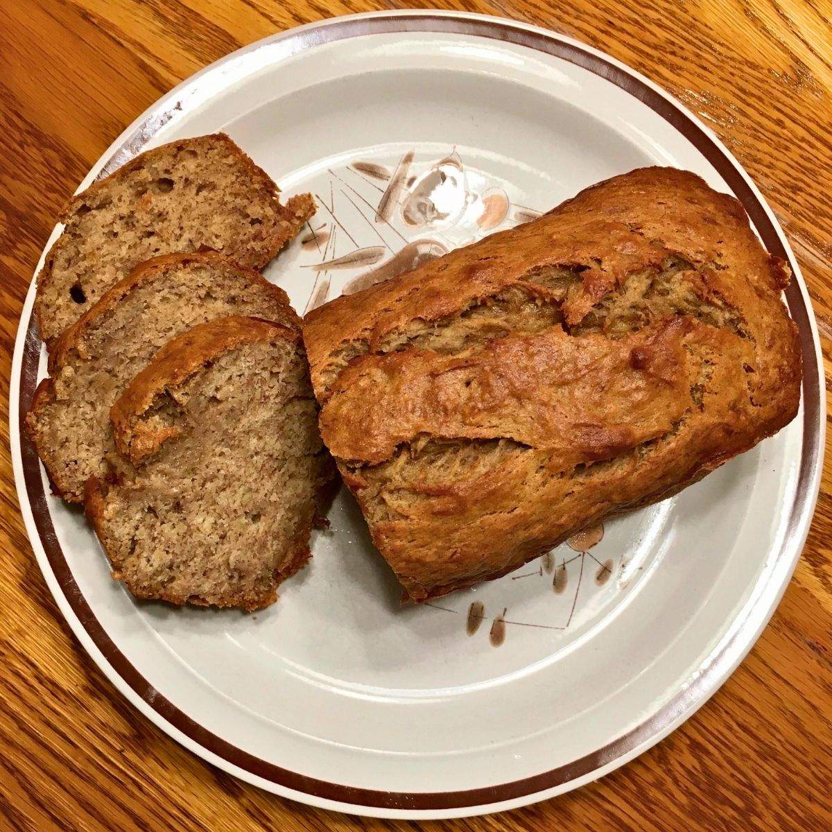 A loaf of golden brown banana bread that is sliced in half. One side is still whole with a crisp, beautiful golden top. The other side is sliced into several pieces of banana bread to show the soft, moist bread.
