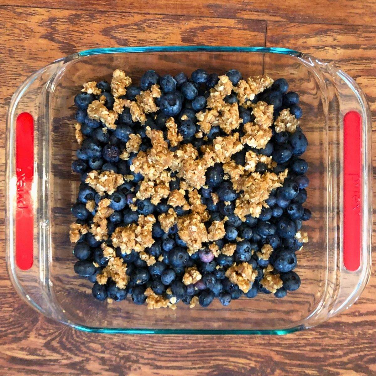 A combination of fresh blueberries and soft oat mixture in a 9x9 glass baking sheet before baking.