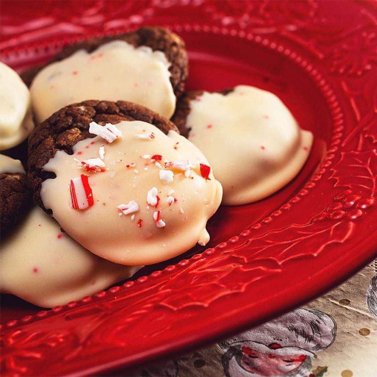 A fancy, red holiday platter with several dark brown chocolate peppermint cookies that are dipped in off white peppermint kisses with spots of red from the candy cane flavor.