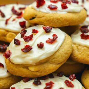 A close up of round Cranberry Bliss Bar Cookies with white, cream frosting on top and chunks of dried cranberries.