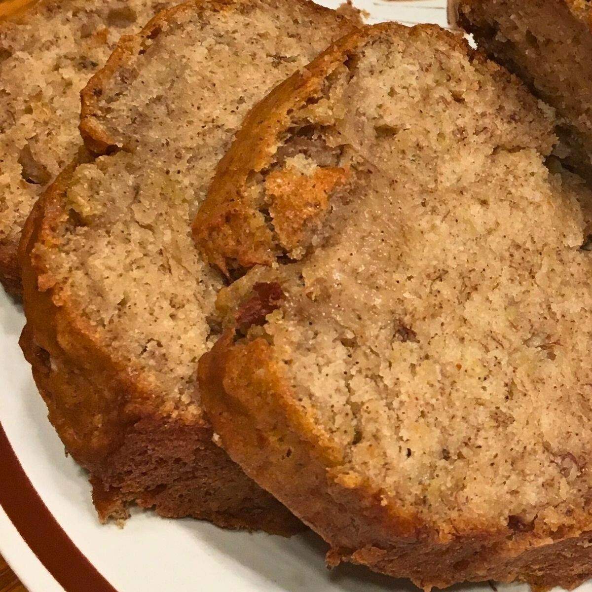 A close-up of tan, soft, moist banana bread slices with specks of brown cinnamon and banana.