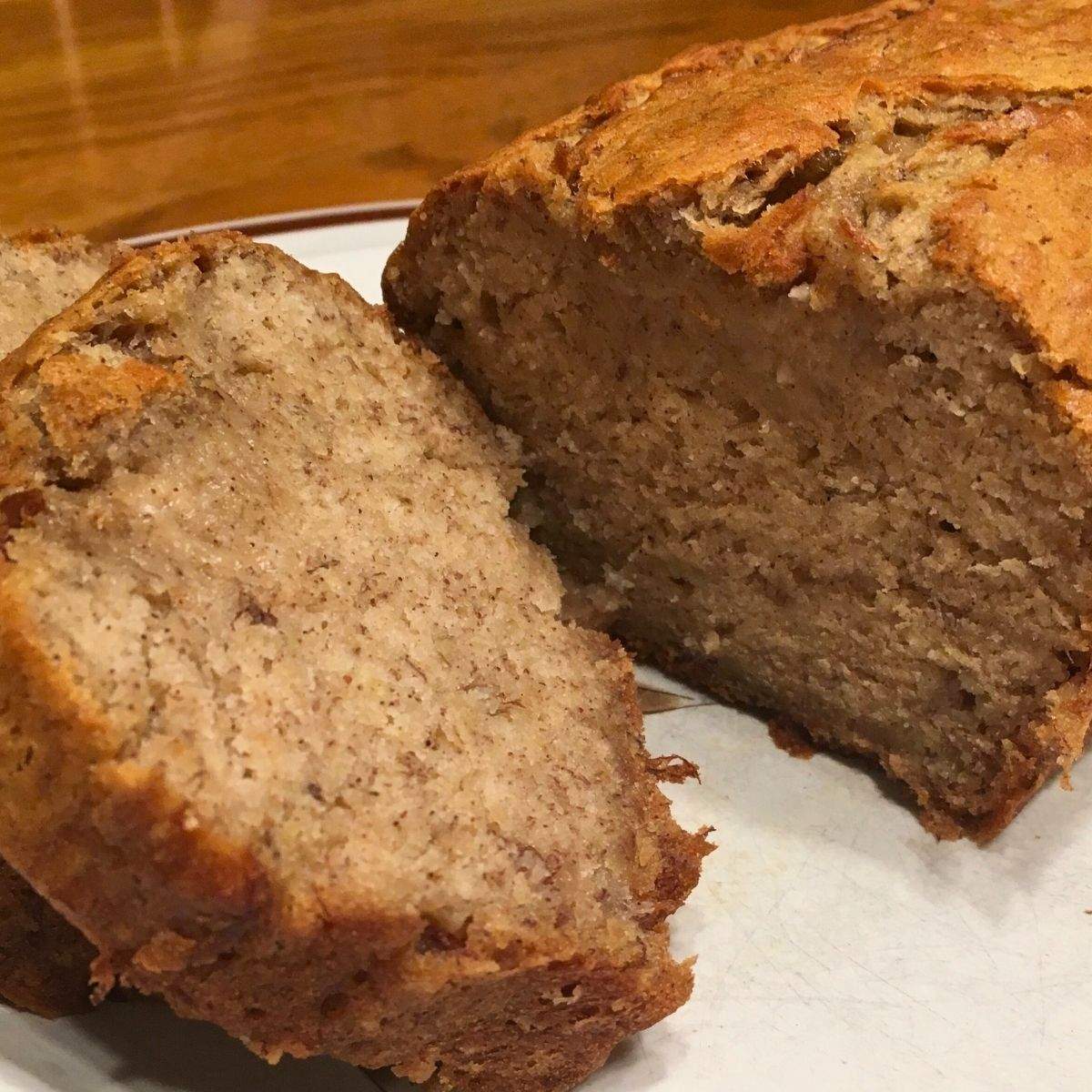 A close-up of sliced, soft, moist banana bread on a white circular plate with a brown outline.