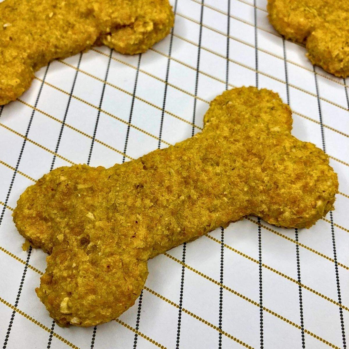 A golden, bone-shaped Cheddar Cheese Dog Treat, next to other Cheddar Cheese Dog Treats, in this Cheesy Dog Biscuit Recipe.