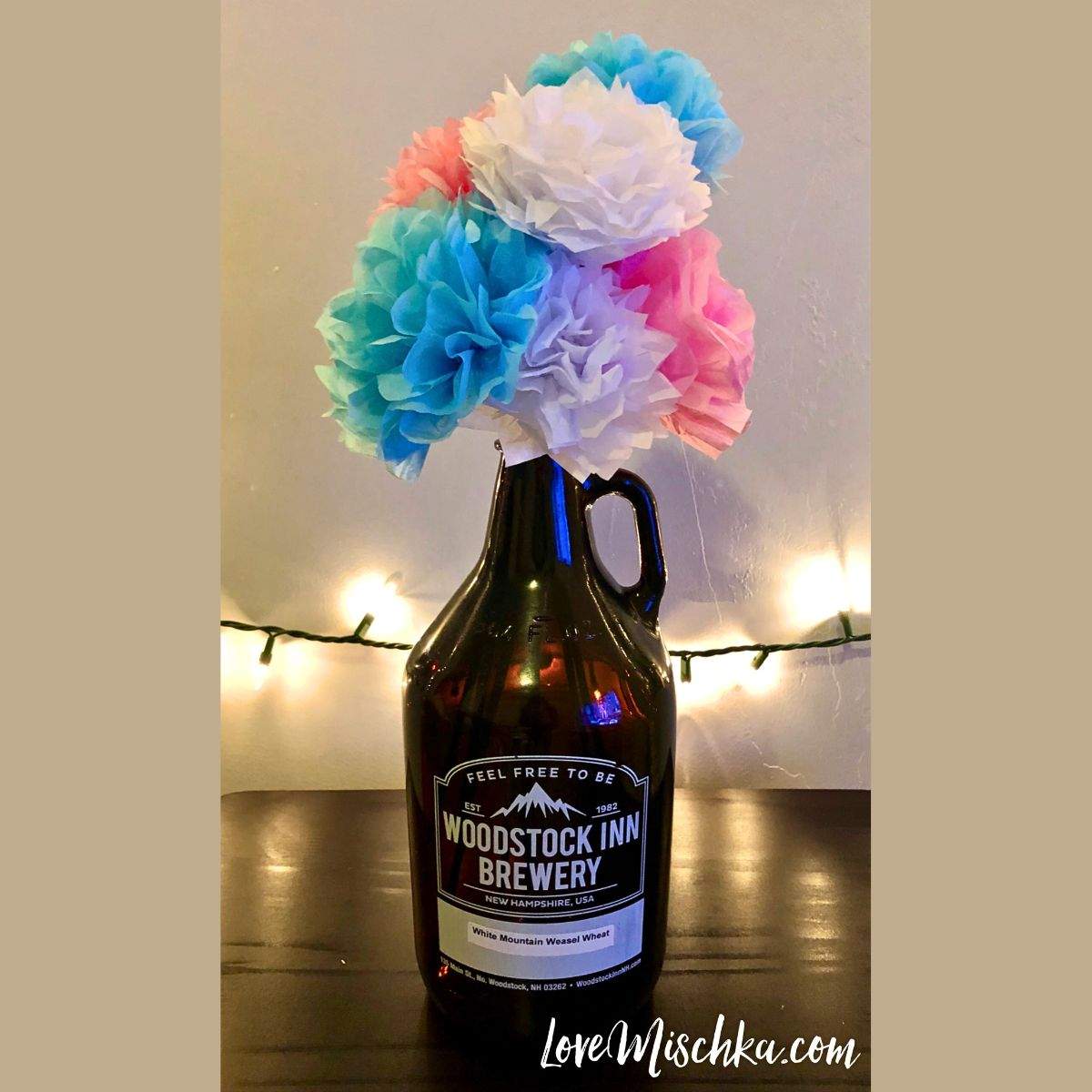 A bouquet of several white, blue, and pink DIY tissue paper flowers in a beer growler.