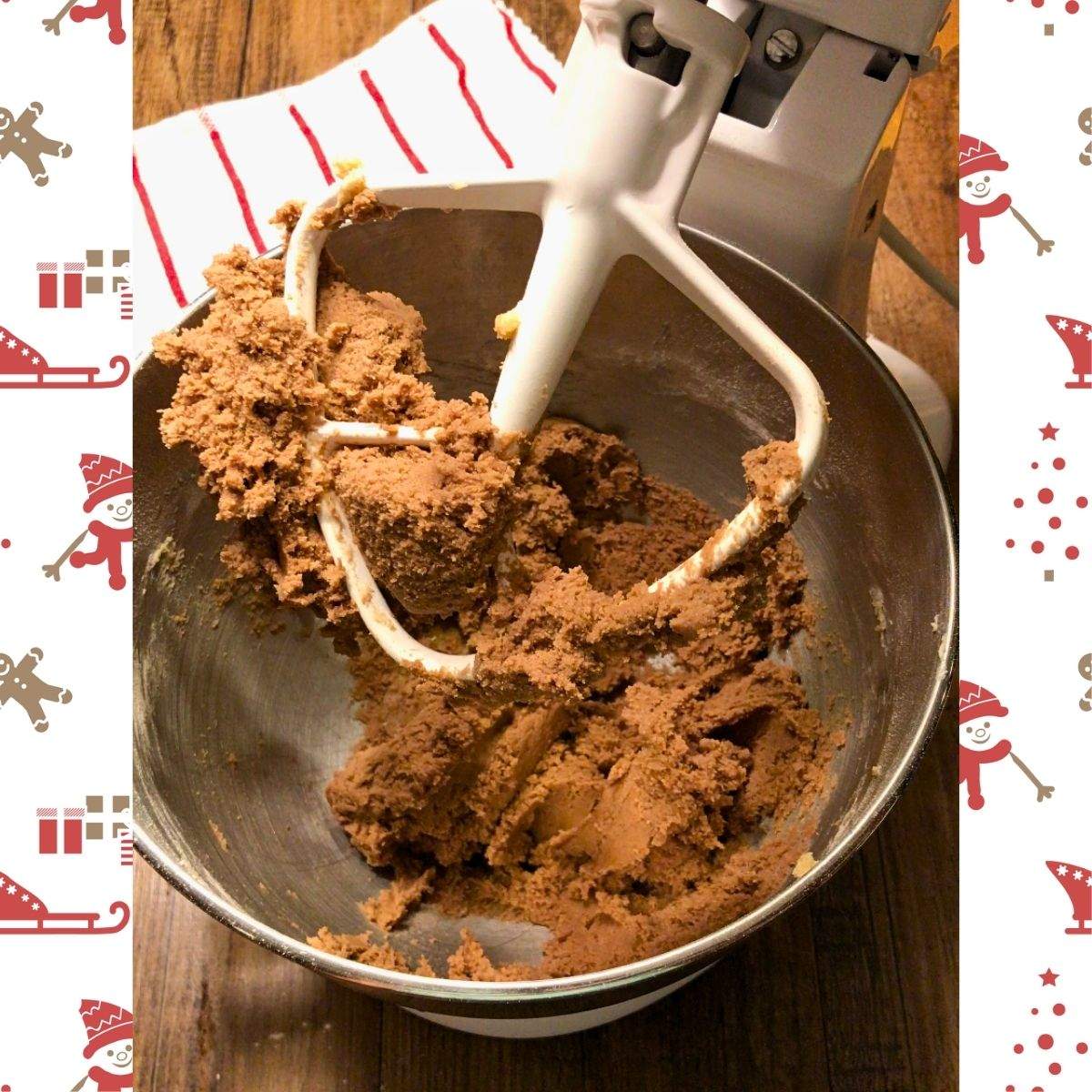 A stand mixer with a paddle attachment opens to show the brown cookie dough of this hot cocoa cookies recipe.