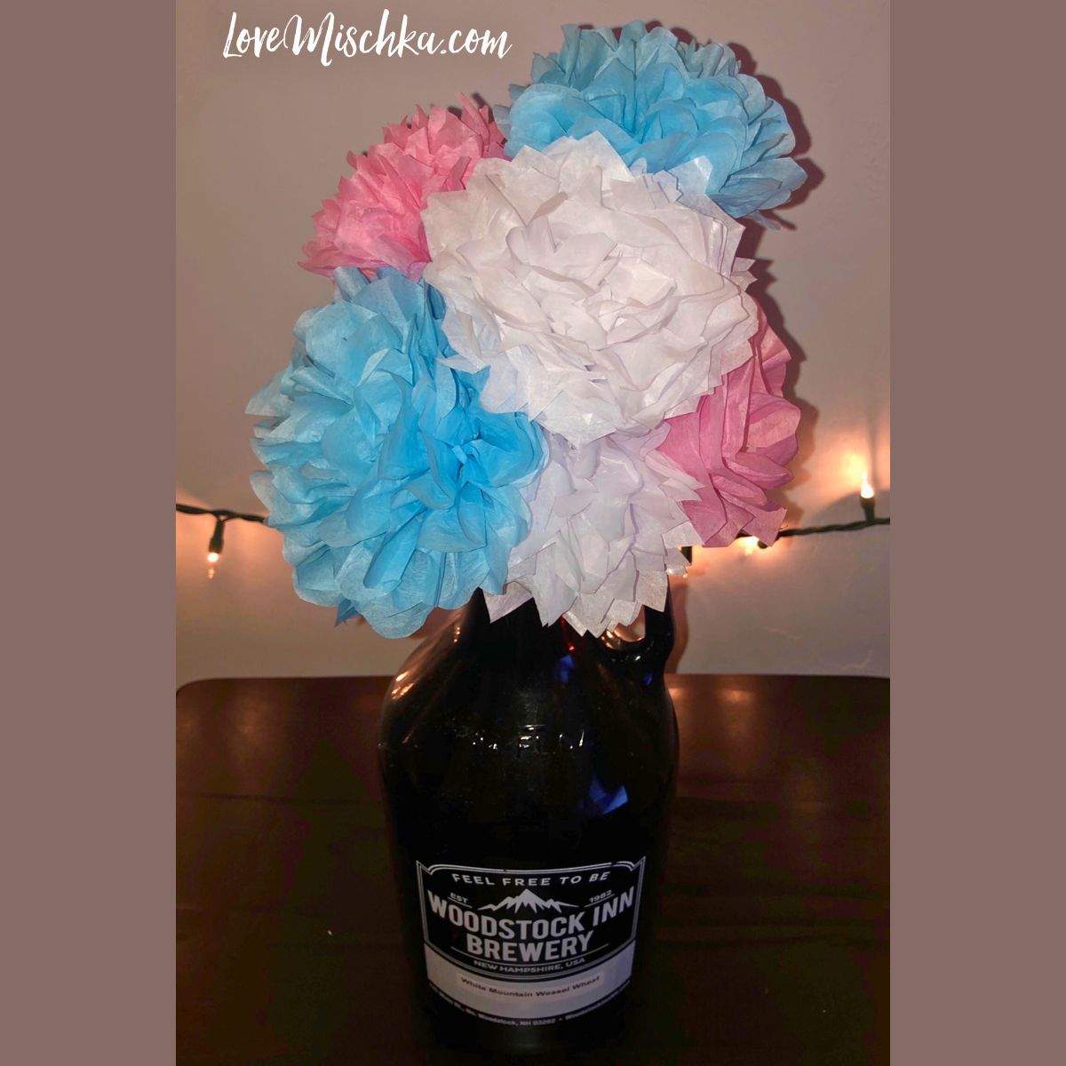 A bouquet of white, baby blue, and light pink tissue paper flower, sticking out of an old beer growler for low key, homemade house decor.