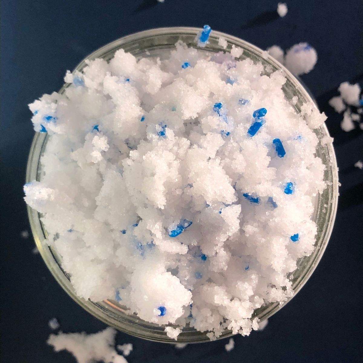 Looking down on a glass mason jar that is overflowing with white, fluffy, homemade sugar scrub with coconut oil and blue sprinkles.