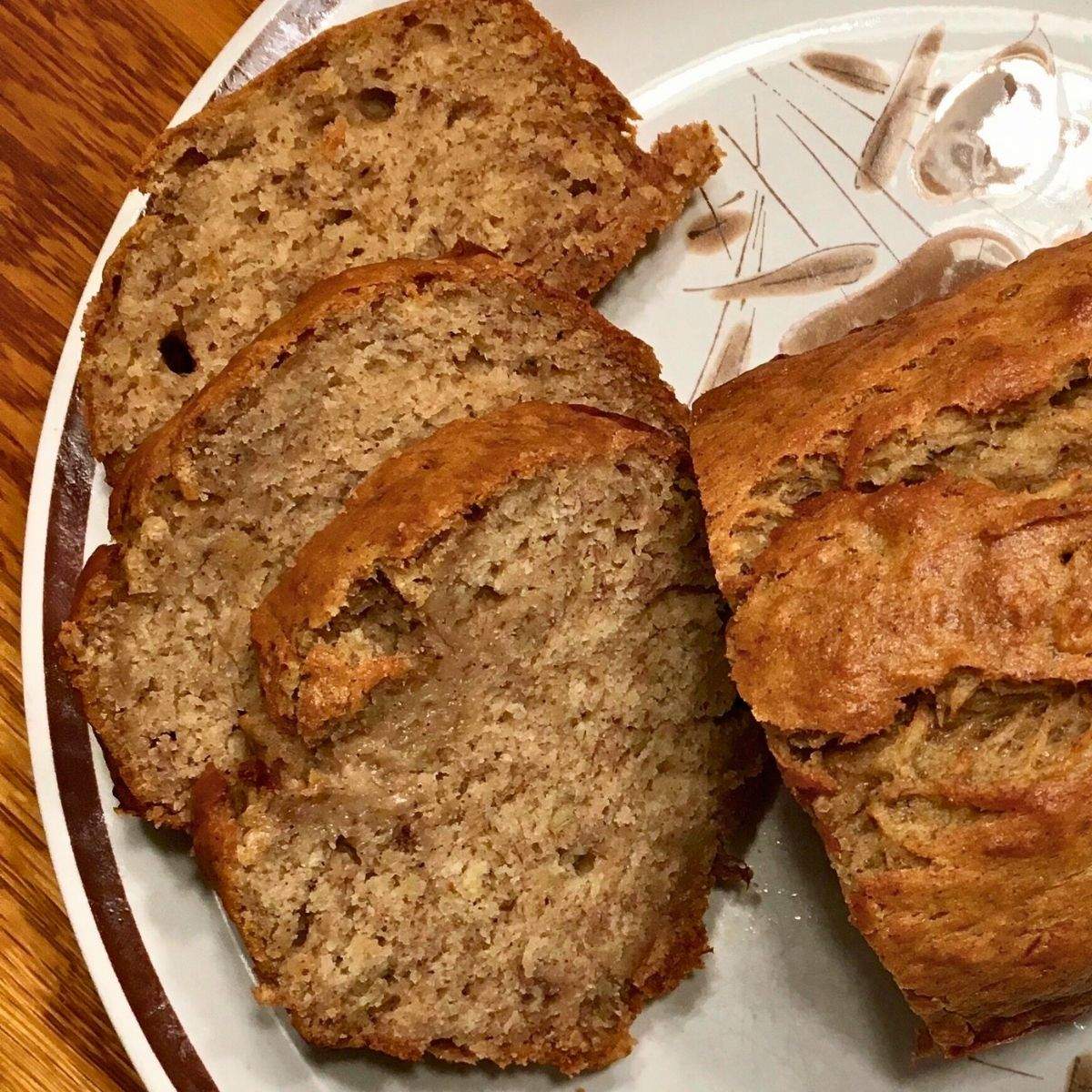 Three slices of brown, baked, delicious, soft, and moist banana bread next to the rest of the load on a 1980s plate.