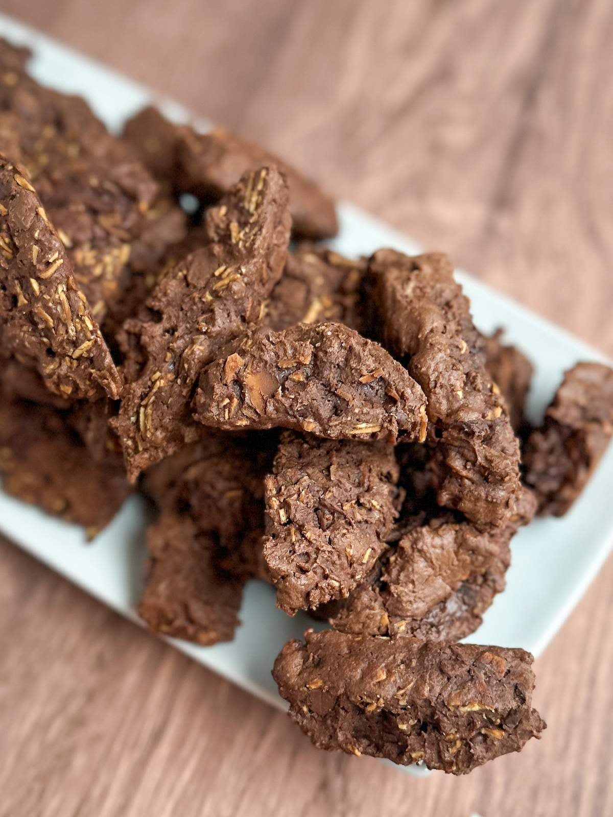 A pile of crispy yet soft, biscotti-shaped, medium brown Italian Chocolate cookies with toasted almond slices on a white rectangular serving dish. 