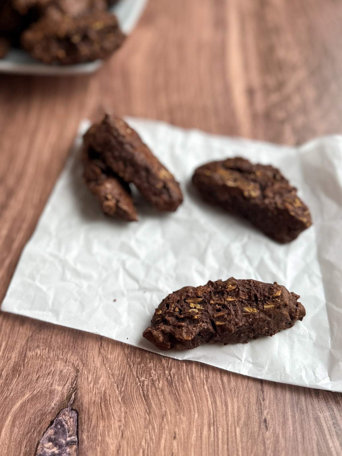 Four biscotti-shaped chocolate cookies with toasted almond slices sit on a folded sheet of parchment paper in this simple, traditional Italian chocolate cookies recipe. 