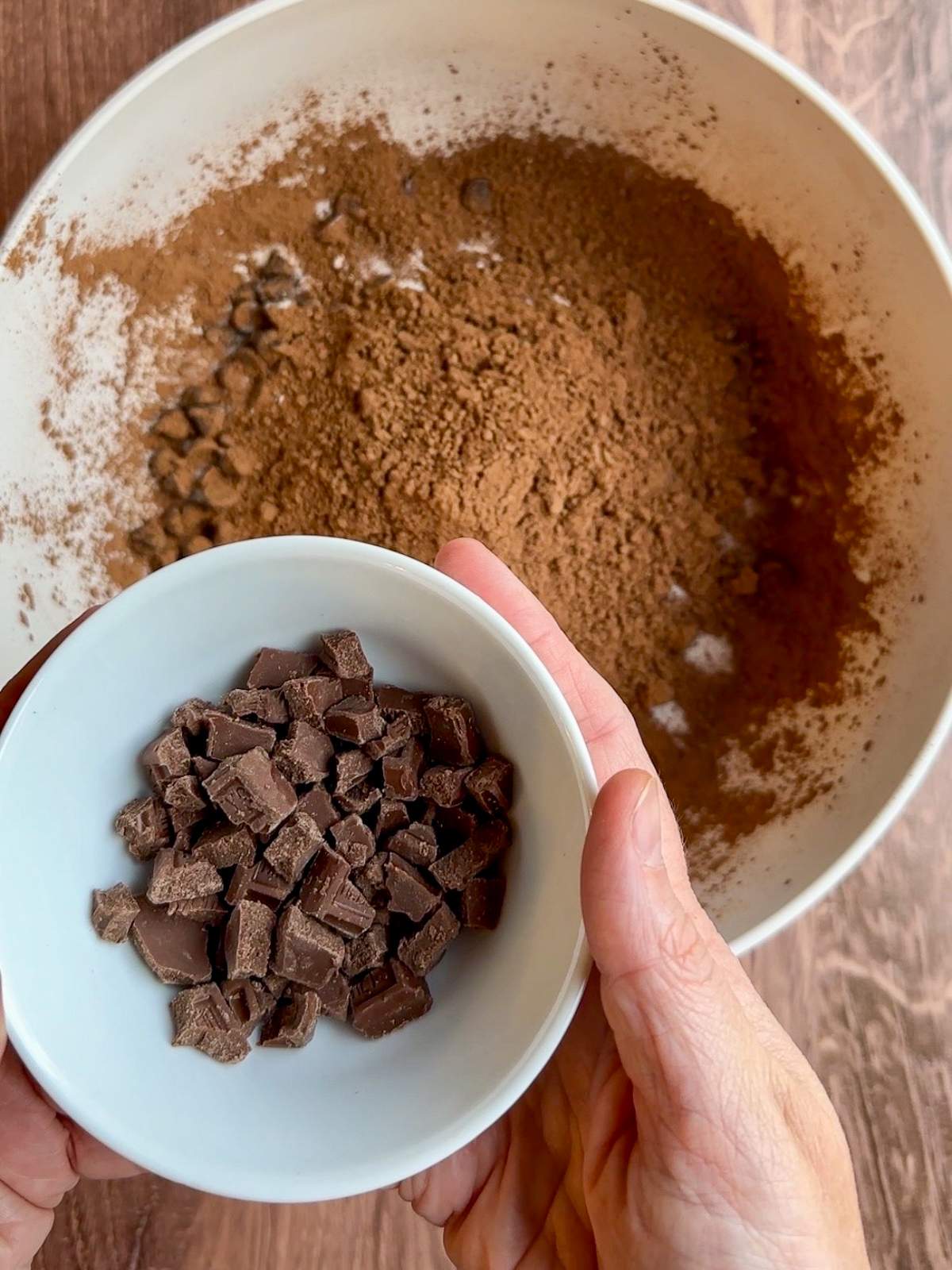 A small bowl of Hershey chocolate candy bar pieces is held above the unmixed ingredients of this italian cookie recipe in a large bowl. 
